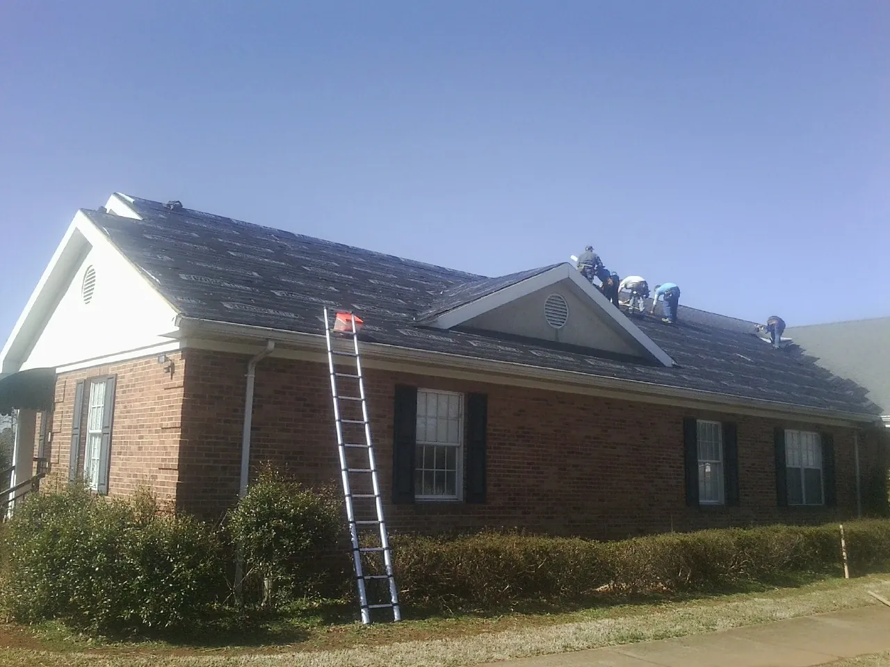 Crew tearing shingles off a brick ranch roof with a ladder set — Emergency Roof Repair work by our crew in Sodus Point