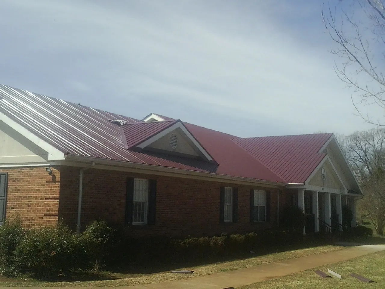Red metal roof with gabled entries on a long brick building, from a Hail Damage Roof Repair job in Sodus Point