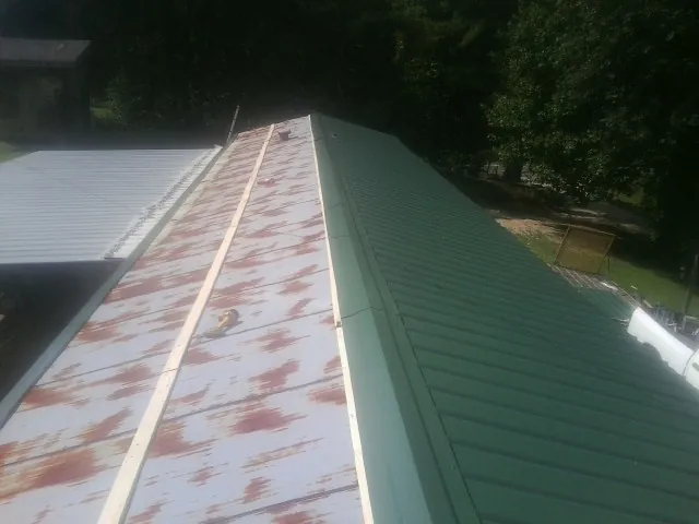 Old rusted panels beside newly installed green metal roofing — Wind Damage Roof Repair by Roofing Brothers in Sodus Point