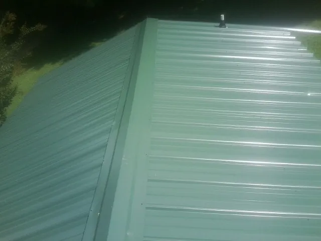 New green metal panels meeting at the ridge of a roof — Flat Roof Repair work by our crew in Sodus Point