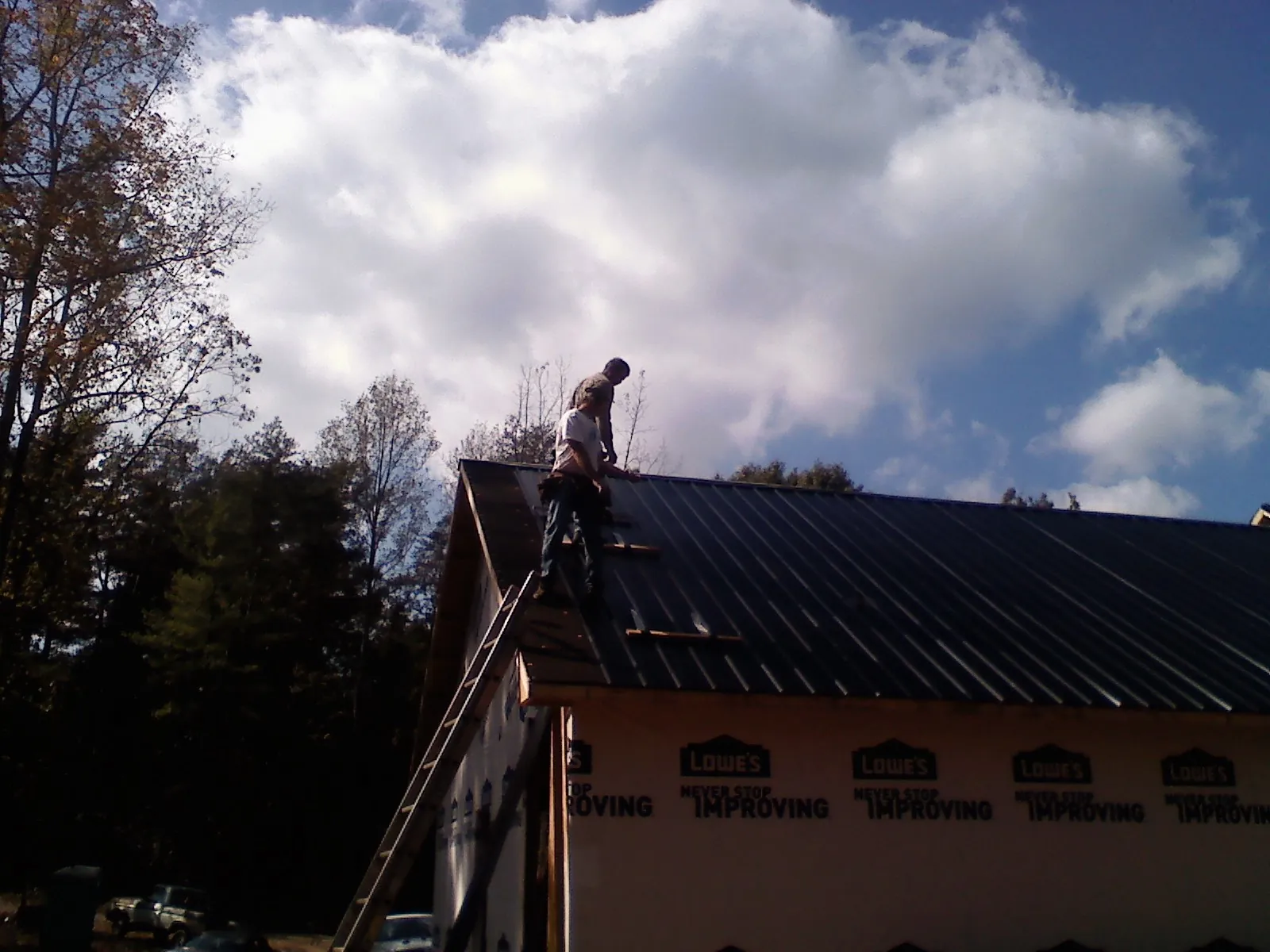 Roofer fastening dark metal panels high against a cloudy sky, from a Roof Inspection job in Sodus Point