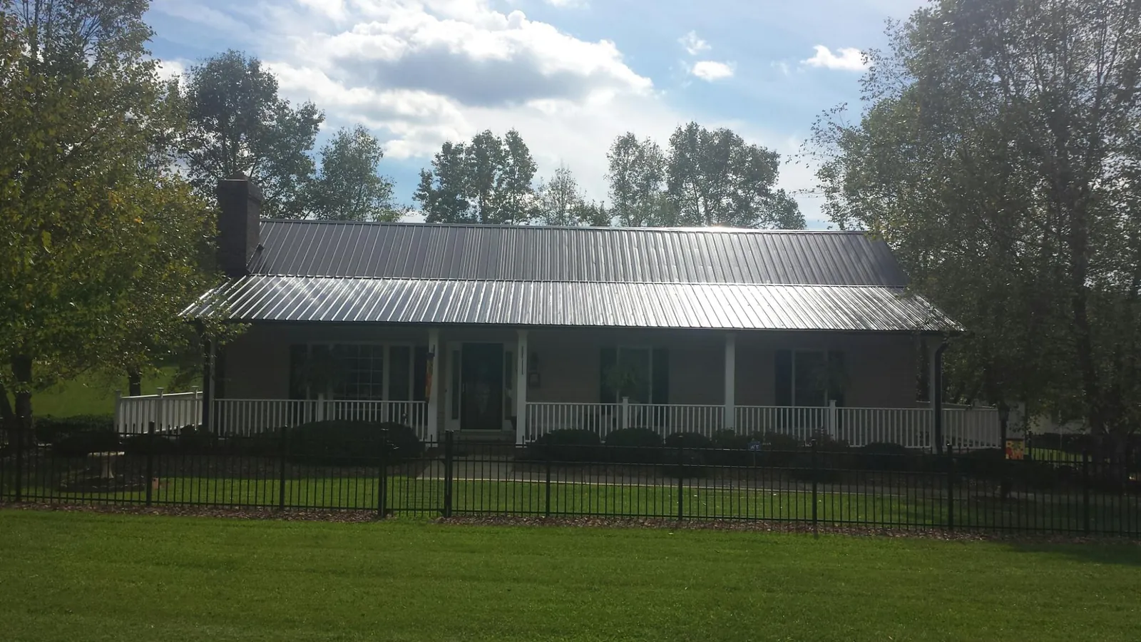 Gray metal roof on a brick ranch with a full width front porch — Gutter Guard Installation work by our crew in Sodus Point