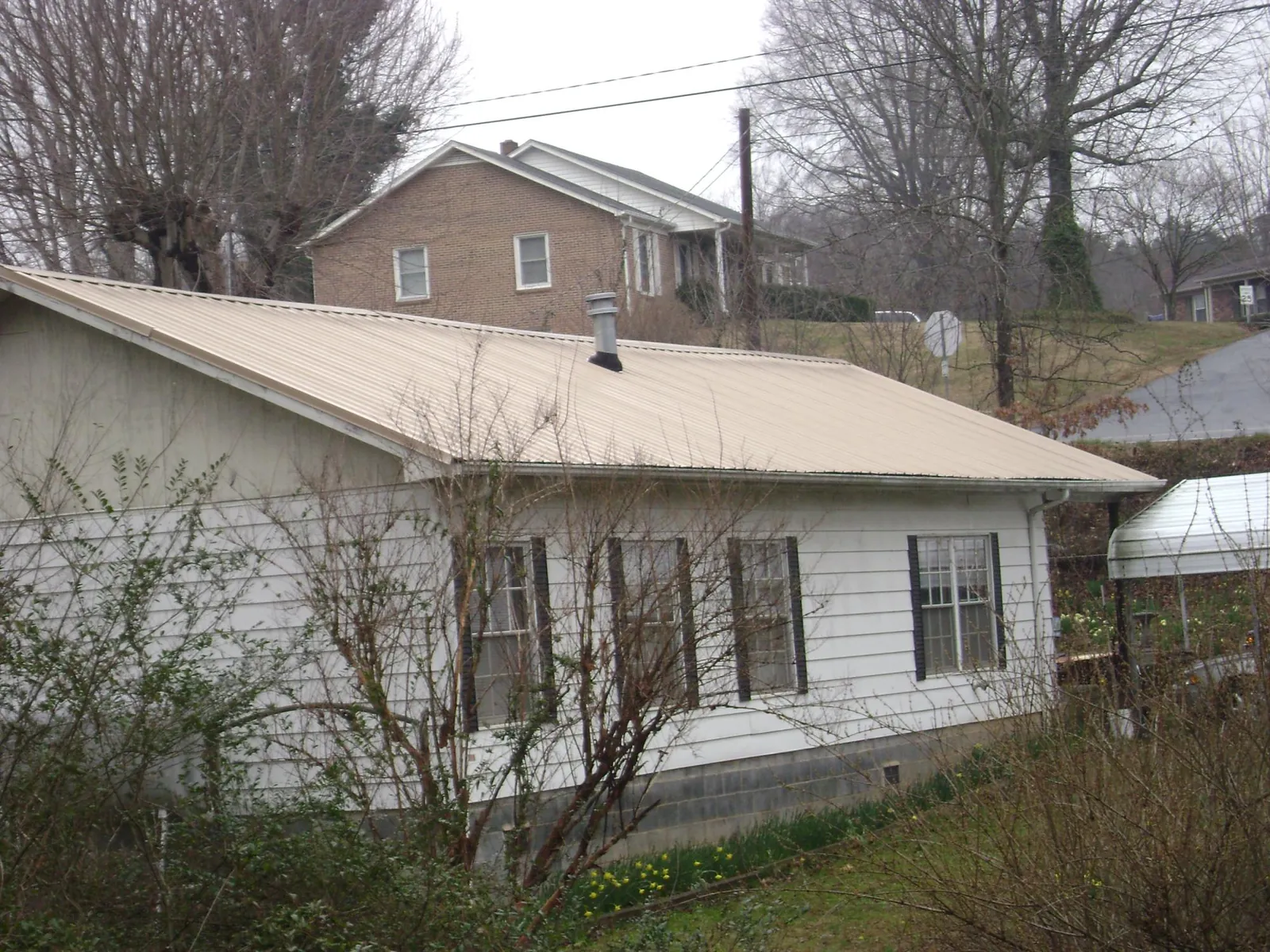 Tan metal roof on a white sided house set into a hillside — Commercial Roofing by Roofing Brothers in Sodus Point