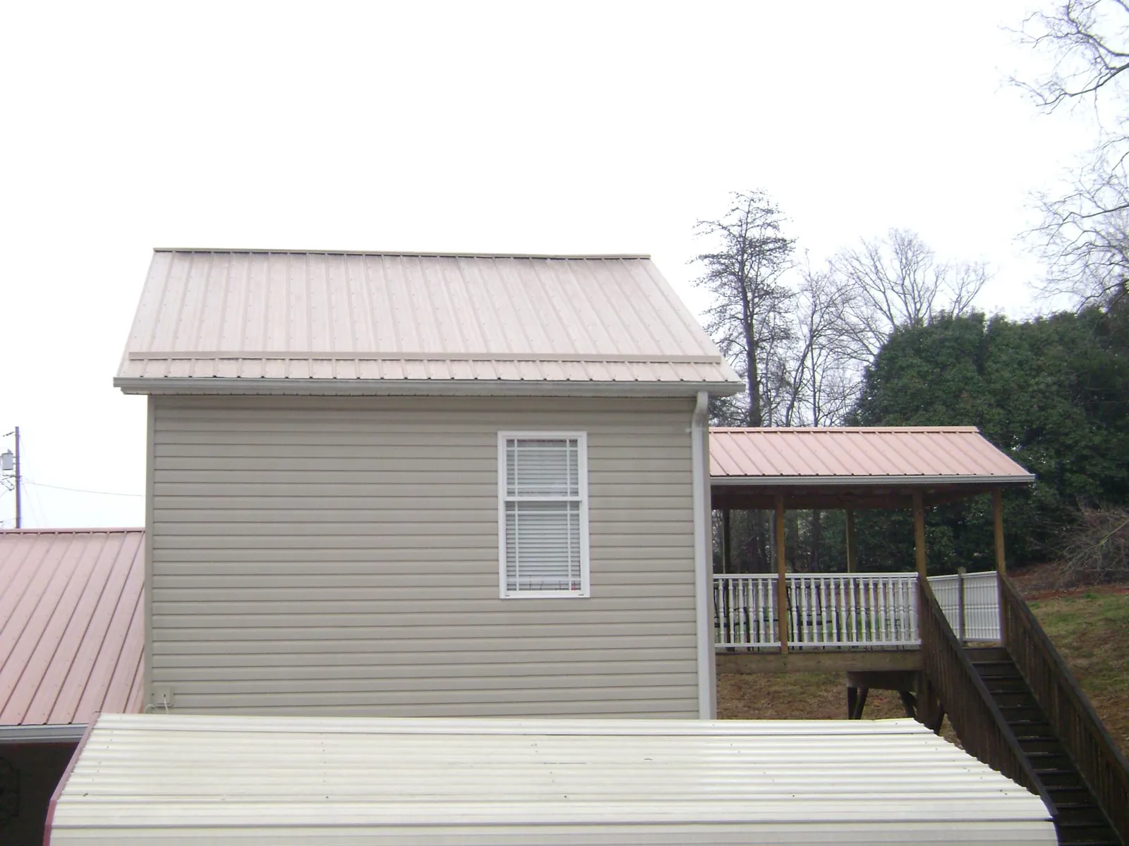Tan metal roofs on a two story addition and attached porch, from a Roof Replacement job in Sodus Point